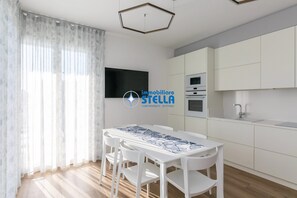 A modern kitchen with white cabinets, a built-in oven, and a white dining table with chairs. - Residence Medusa - 15 (Lido di Jesolo)