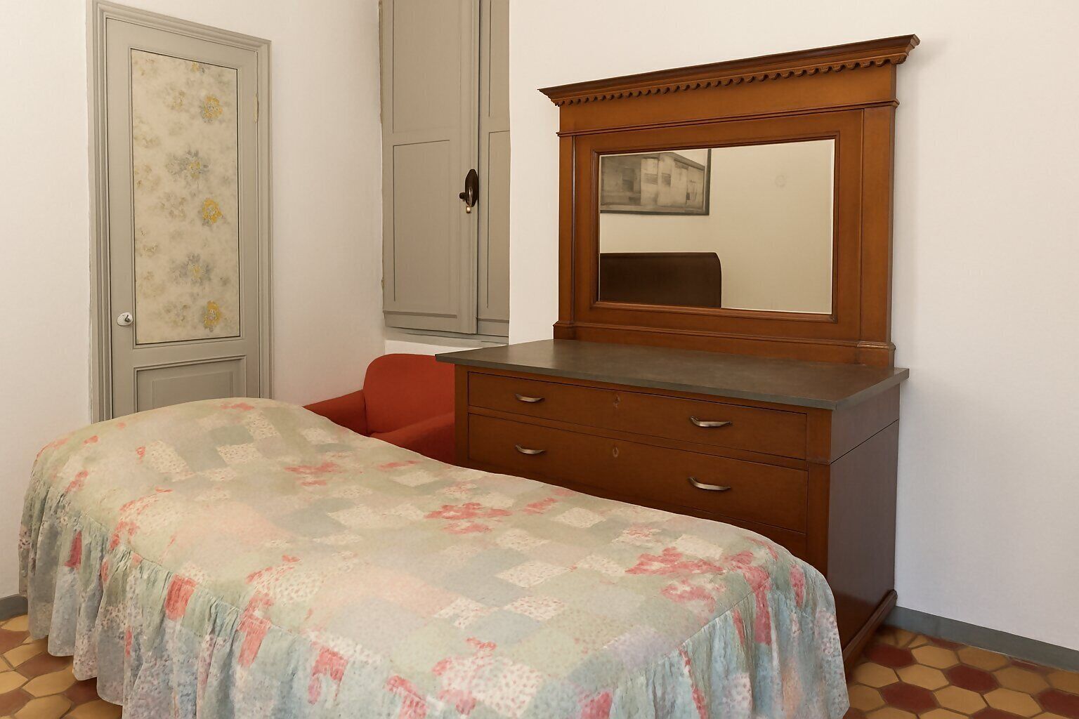 Un dormitorio con una cama, un tocador, un espejo y una puerta con diseño floral.