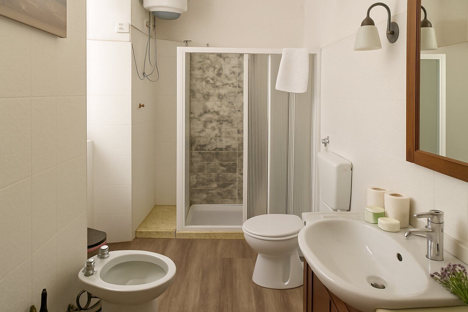 Une salle de bain équipée d’une douche, de toilettes, d’un bidet, d’un lavabo et d’un miroir.