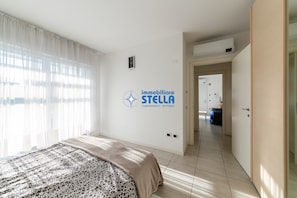 A hotel room with a bed, a wall-mounted air conditioner, a door leading to a hallway, and a logo on the wall. - Laguna Park °Pool°- 05 (Lido di Jesolo)
