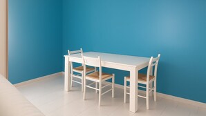 Una mesa blanca y cuatro sillas en una habitación con pared azul y suelo blanco.