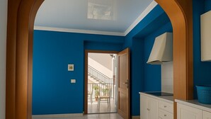 Un pasillo con pared azul, una puerta de madera y vista hacia un balcón.