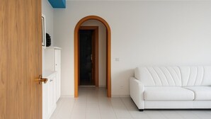 Una habitación con un sofá blanco, una puerta de madera y un suelo de baldosas.