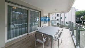 Een balkon met een tafel en stoelen, grote schuiframen en uitzicht op gebouwen.