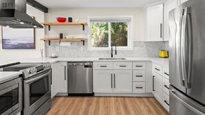 Una cucina moderna con mobili bianchi, elettrodomestici in acciaio inossidabile, lavastoviglie e una finestra vista su un'area verde.