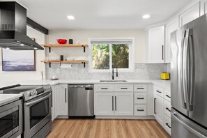 Una cocina moderna con armarios blancos, electrodomésticos de acero inoxidable, lavavajillas y ventana con vistas a zonas verdes.