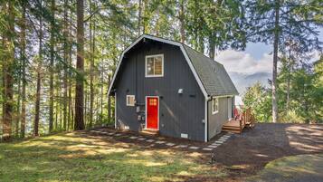 Une cabane rustique avec une porte rouge, un petit porche et une vue sur la forêt environnante.