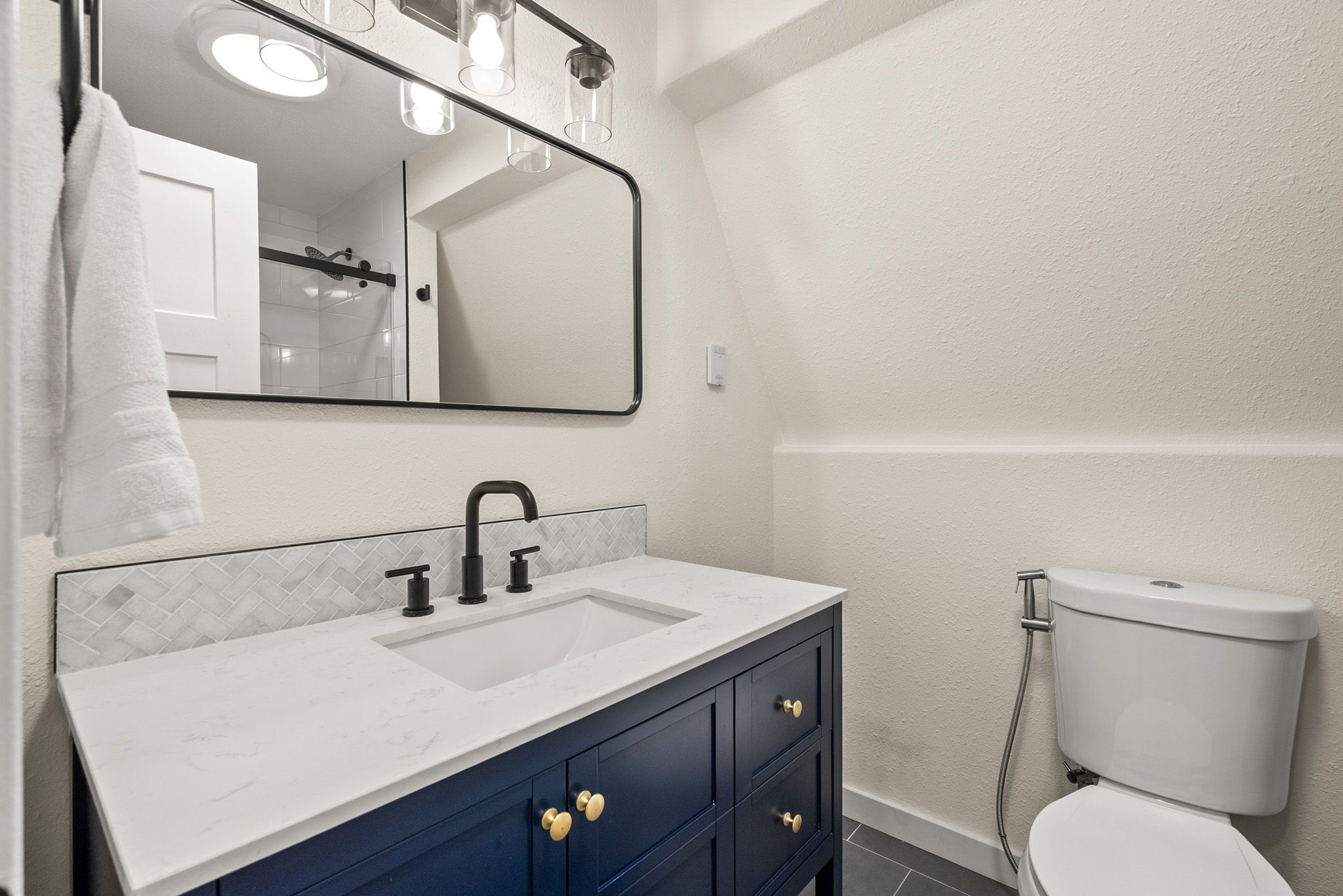 A bathroom with a white sink, dark blue cabinets, a mirror, and a toilet.