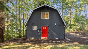 Una baita di legno scuro con una porta rossa, immersa tra gli alberi.