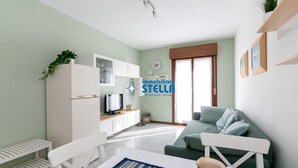 Ein Wohnzimmer mit einer Couch, einem Fernseher, einem Esstisch mit einer Kaffeetasse und einem Bücherregal.