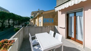 Ein Balkon mit weißem Tisch und Stühlen, einer Schiebetür aus Glas und Blick auf die Straße.