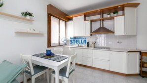 Eine moderne Küche mit weißen Schränken, Holzregalen und einer Essecke mit Tisch und Stühlen.