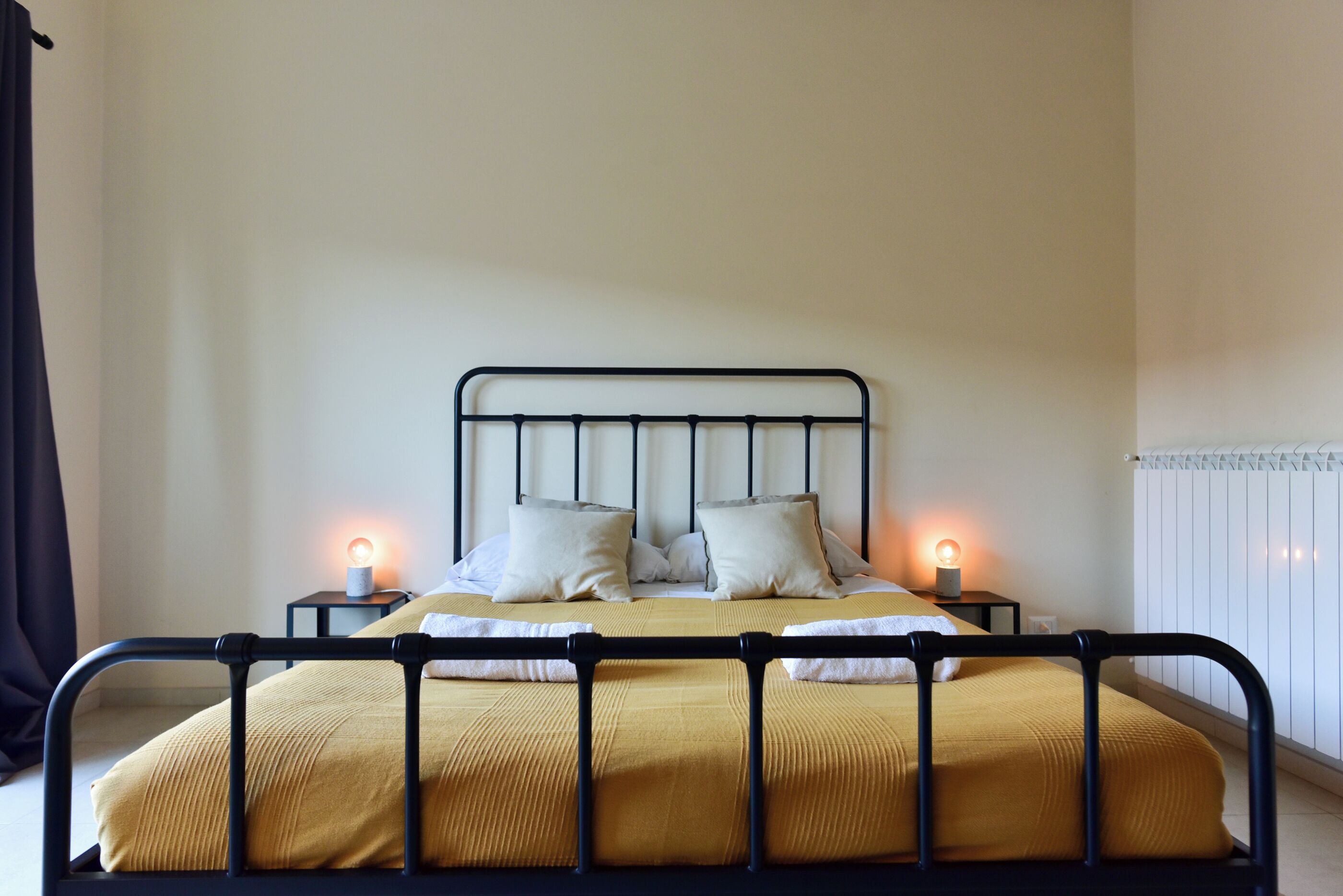 A bed with a metal frame, two bedside tables with lamps, and a radiator on the wall.