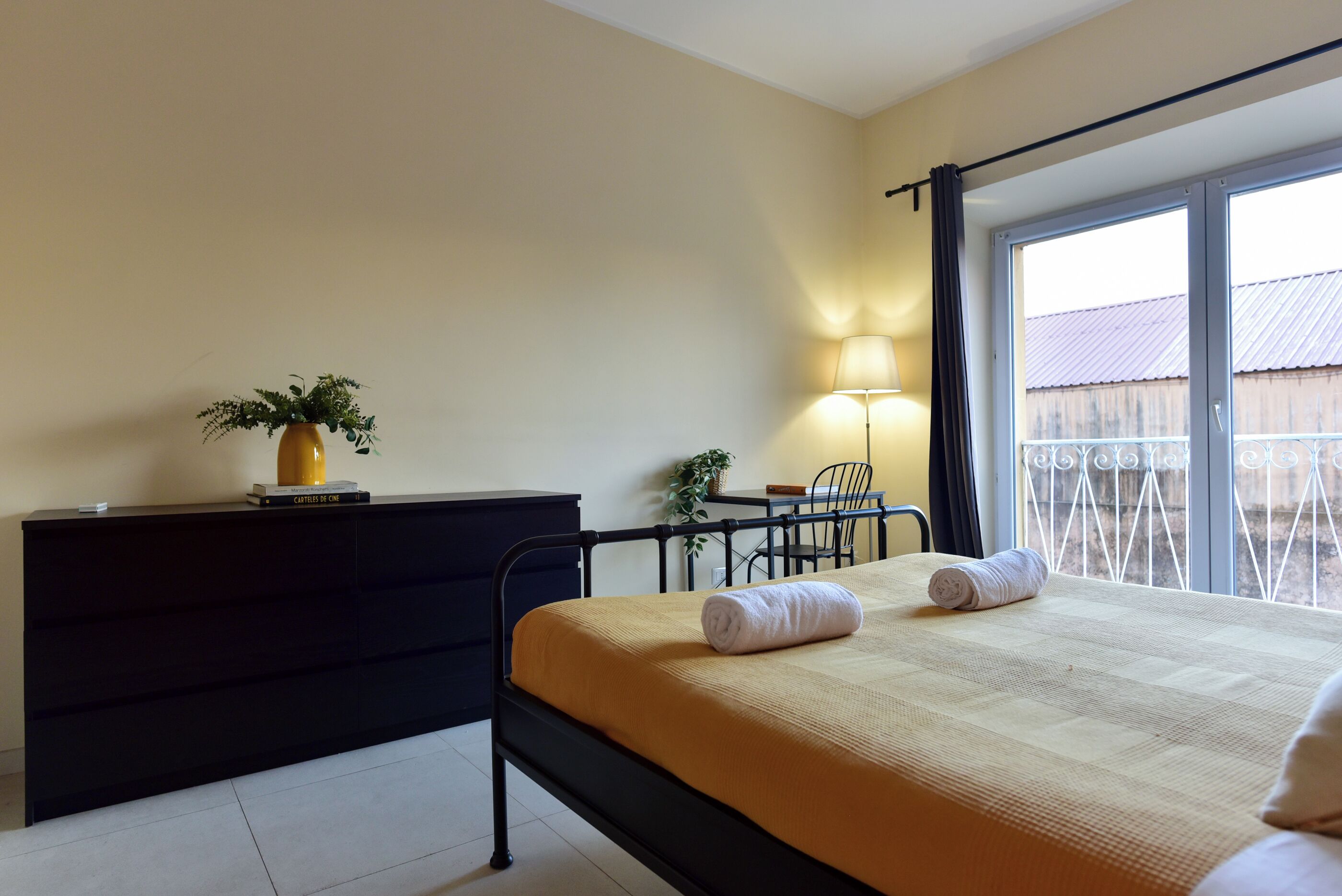 A bedroom with a bed, bedside table, lamp, and a view through a window.