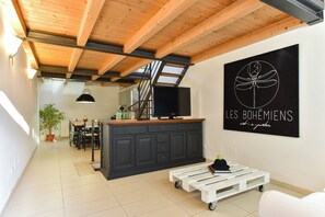 A modern interior with a wooden ceiling, a black cabinet with a television, a white pallet table, and a wall art piece. - 4BNB - San Lorenzo Spacious Apartment (Rome)