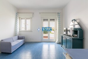 Ein Zimmer mit einer Couch, einer Küchenzeile und einer Schiebeglastür, die nach draußen führt.
