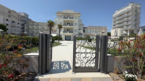 A gated entrance to a residential building complex with multiple balconies and a clear sky. - Residence ° Bagni Miramare °- 6 (Lido di Jesolo)
