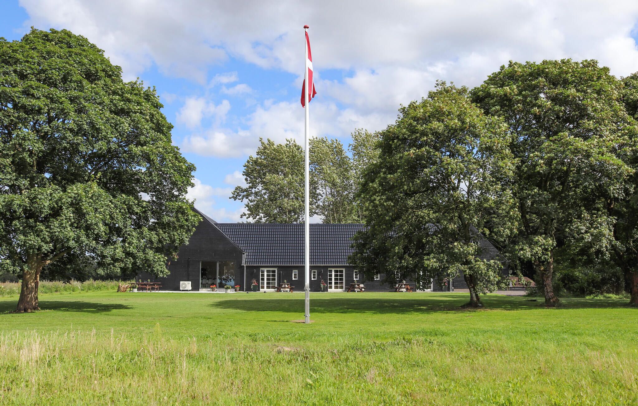 A building with a flagpole, surrounded by trees and a grassy field.