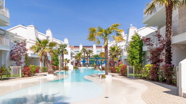 Un complex turístic amb piscina, palmeres i edificis de color blanc.