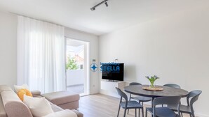 Un saló modern amb un sofà, una taula de dinar amb cadires i un televisió de pantalla plana penjada a la paret.