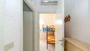 En smal hallgång med en våningssäng i bakgrunden, en träbänk och en väggmonterad luftkonditioneringsanläggning.