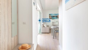 En hall med en trädörr, en hatt som ligger på golvet, en soffa och en matplats med stolar.