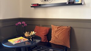 Een moderne woonkamer met een flatscreen televisie aan de muur, een tafeltje met een boek, een bankje en decoratieve bloemen.