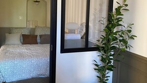 Een hotelkamer met een bed, een plant in pot, een spiegel en een raam met gordijnen.