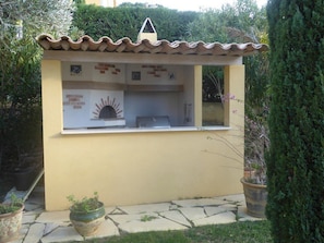 A small outdoor kitchen with a tiled roof, a brick oven, and a window. - VILLA WITH BEAUTIFUL SEA VIEW AND SWIMMING POOL TO RENT FOR 8 PEOPLE IN SAINTTE-MAXIME (STE MAXIME)
