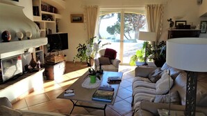 Ein Wohnzimmer mit Sofa, Couchtisch, Fernseher, Bücherregal und Blick ins Freie.