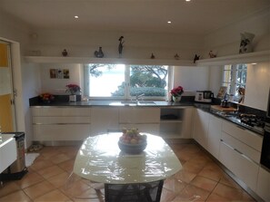 A kitchen with a dining table covered with plastic, a window with a view, and various kitchen appliances. - VILLA WITH BEAUTIFUL SEA VIEW AND SWIMMING POOL TO RENT FOR 8 PEOPLE IN SAINTTE-MAXIME (STE MAXIME)