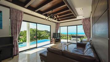 A modern living room with a large sofa, a television, and a view of a swimming pool and ocean.