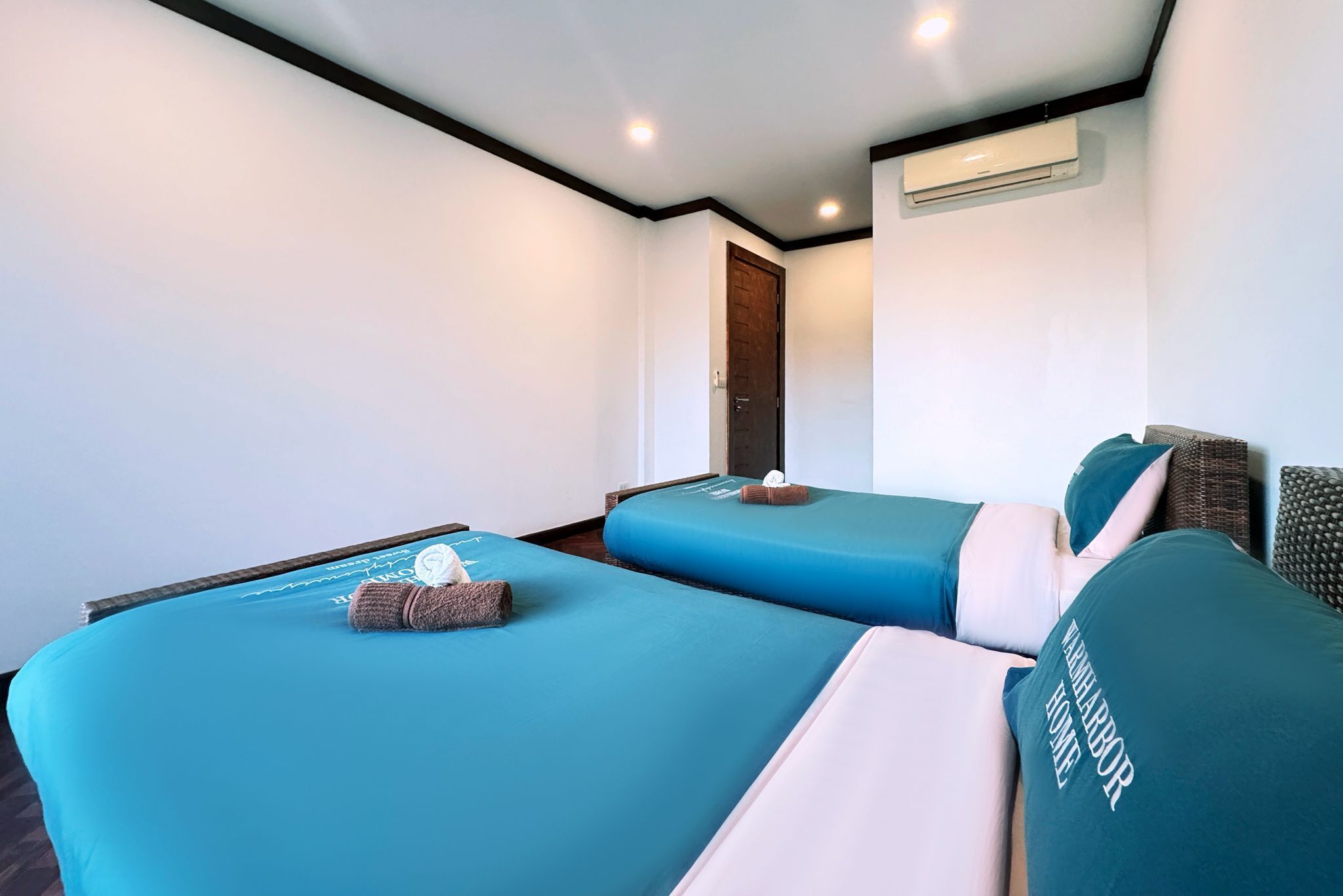 Een hotelkamer met twee bedden, een deur, een airconditioning en een kleine handdoek op een van de bedden.