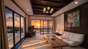 A modern living room with a sofa, a coffee table, and a TV. There is a large window with a view of the sunset. - Bangpor Seaview Nice Villa (Koh Samui)