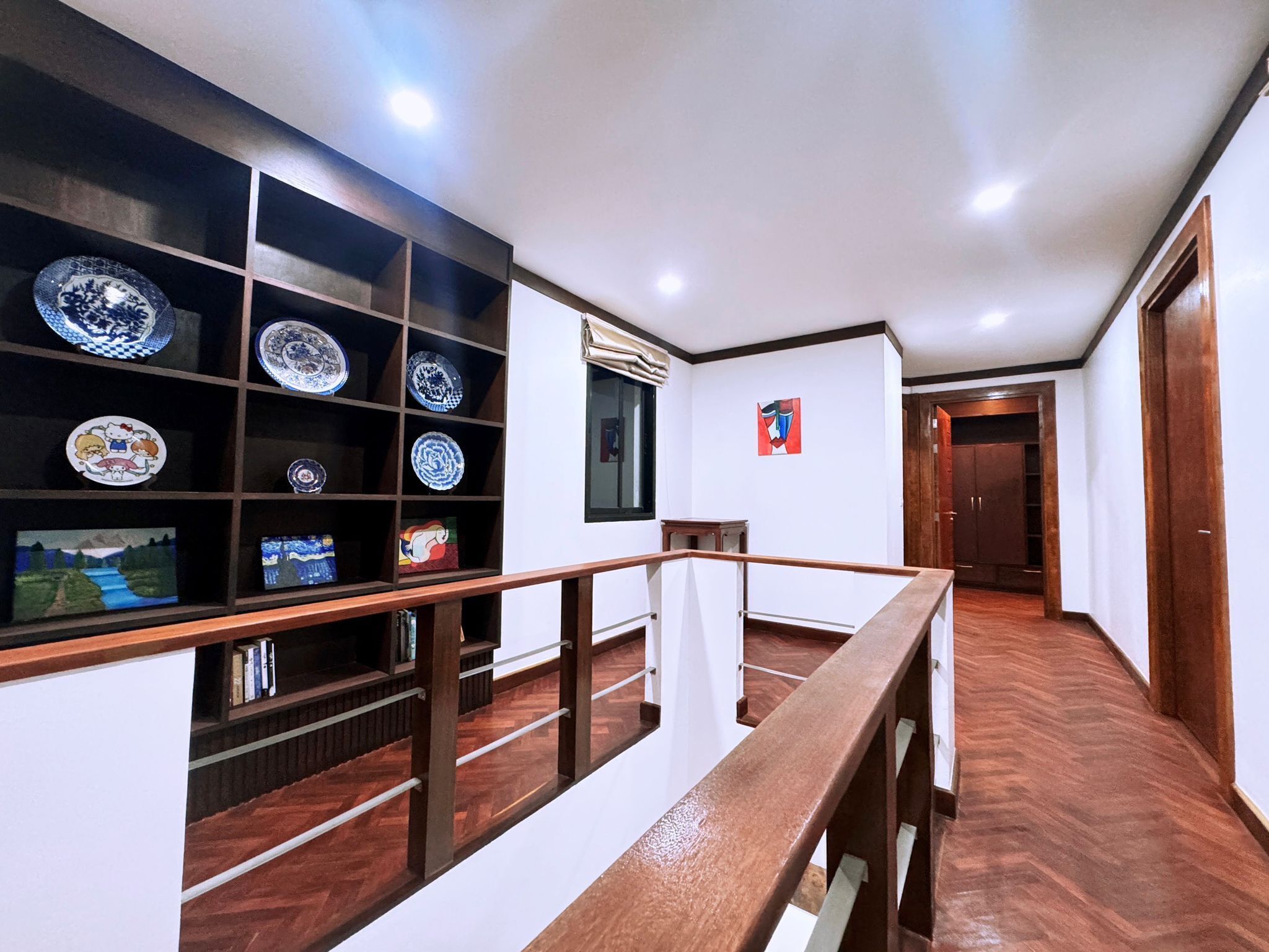 A hallway with a wooden railing, a wall-mounted shelf with decorative plates, and a door at the end.