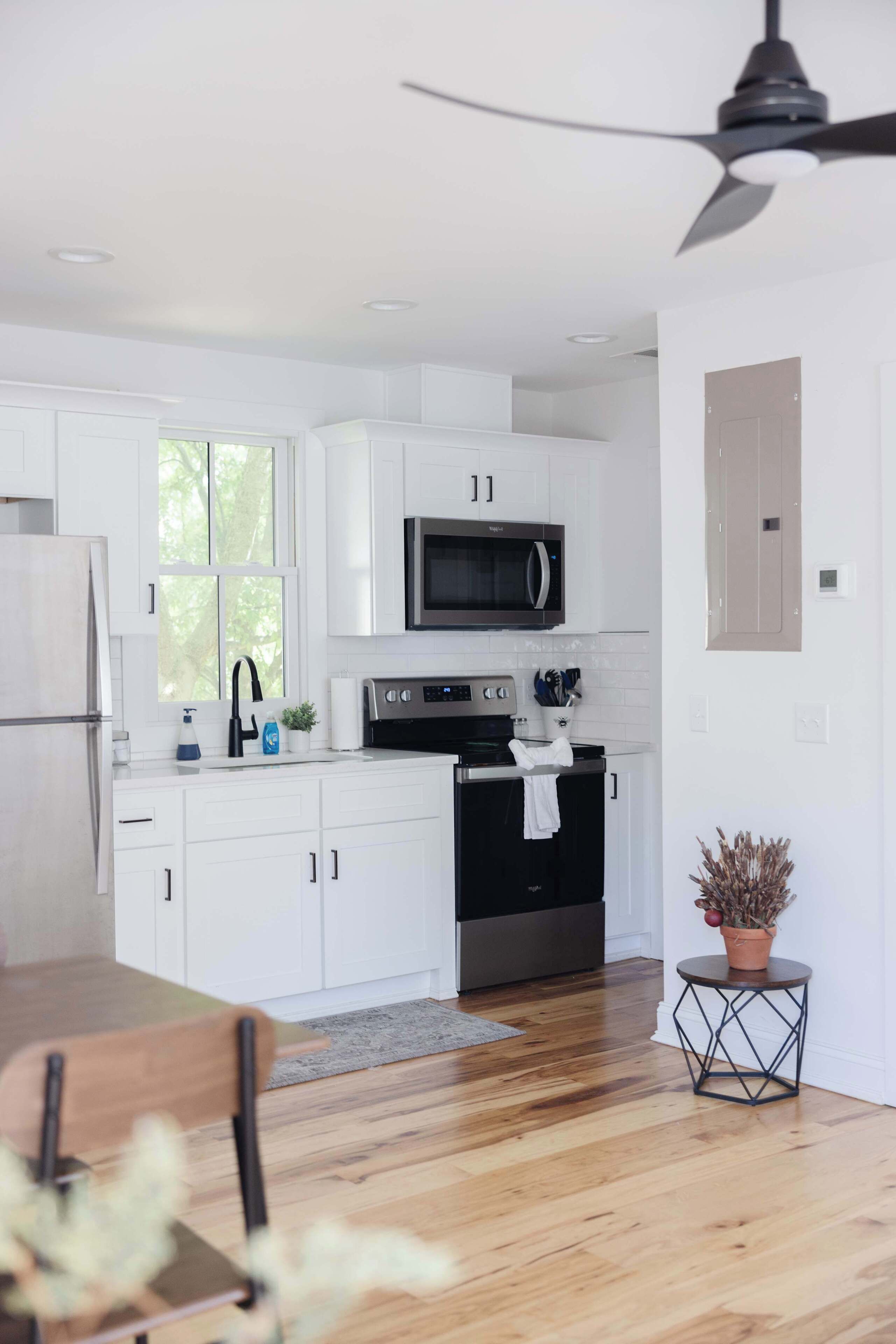 A modern kitchen with white cabinets, a microwave, an oven, and a ceiling fan.