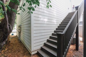 Una escalera con barandal negro que sube hacia una pared exterior blanca.