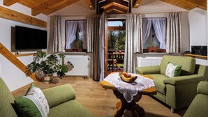 Un soggiorno accogliente con soffitto in legno, divani verdi, un tavolo con della frutta e una televisione.