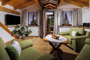 A cozy living room with a wooden ceiling, green sofas, a table with fruit, and a TV. - Vacation apartment Hoher Göll for 2-5 persons, approx. 110 sqm, 2 bedrooms, living room, kitchen, balcony (Bischofswiesen)