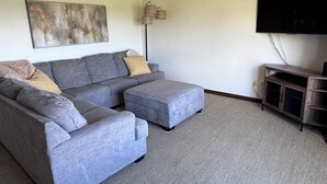 A living room with a grey sectional sofa, a flat-screen TV, a floor lamp, and a painting on the wall. - Water View Home Near West Beach (Coupeville)