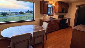 A kitchen with wooden cabinets, a dining table with chairs, a window with a view of a landscape, and a skylight. - Water View Home Near West Beach (Coupeville)