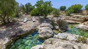 Paisagem rochosa com águas cristalinas, árvores e espreguiçadeiras.