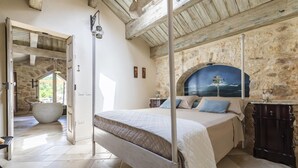 Quarto com cama, paredes de pedra, um mural e vista para o exterior.