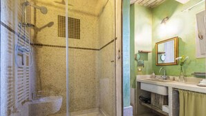 Casa de banho com chuveiro de cabine em vidro, lavatório com espelho e parede verde.