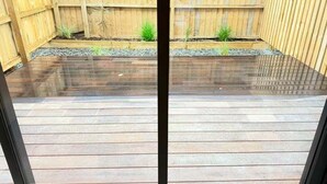 Una terraza de madera con baranda metálica, rodeada por una valla de madera y pequeñas plantas.
