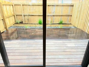 Une terrasse en bois avec une rambarde en métal, entourée d’une clôture en bois et de petites plantes.