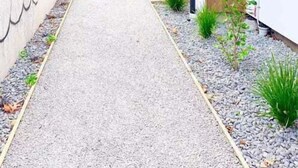 Un sendero estrecho flanqueado por edificios, con un muro de concreto a un lado y una puerta de madera al otro.