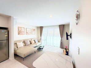 Un salon moderne avec un canapé, une table basse et une table à manger. On y trouve également un réfrigérateur, une horloge au mur et une fenêtre avec des rideaux.