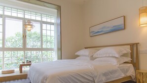 Un dormitorio con un ventanal grande, una cama con ropa blanca, una mesita de noche y una lámpara de pared.