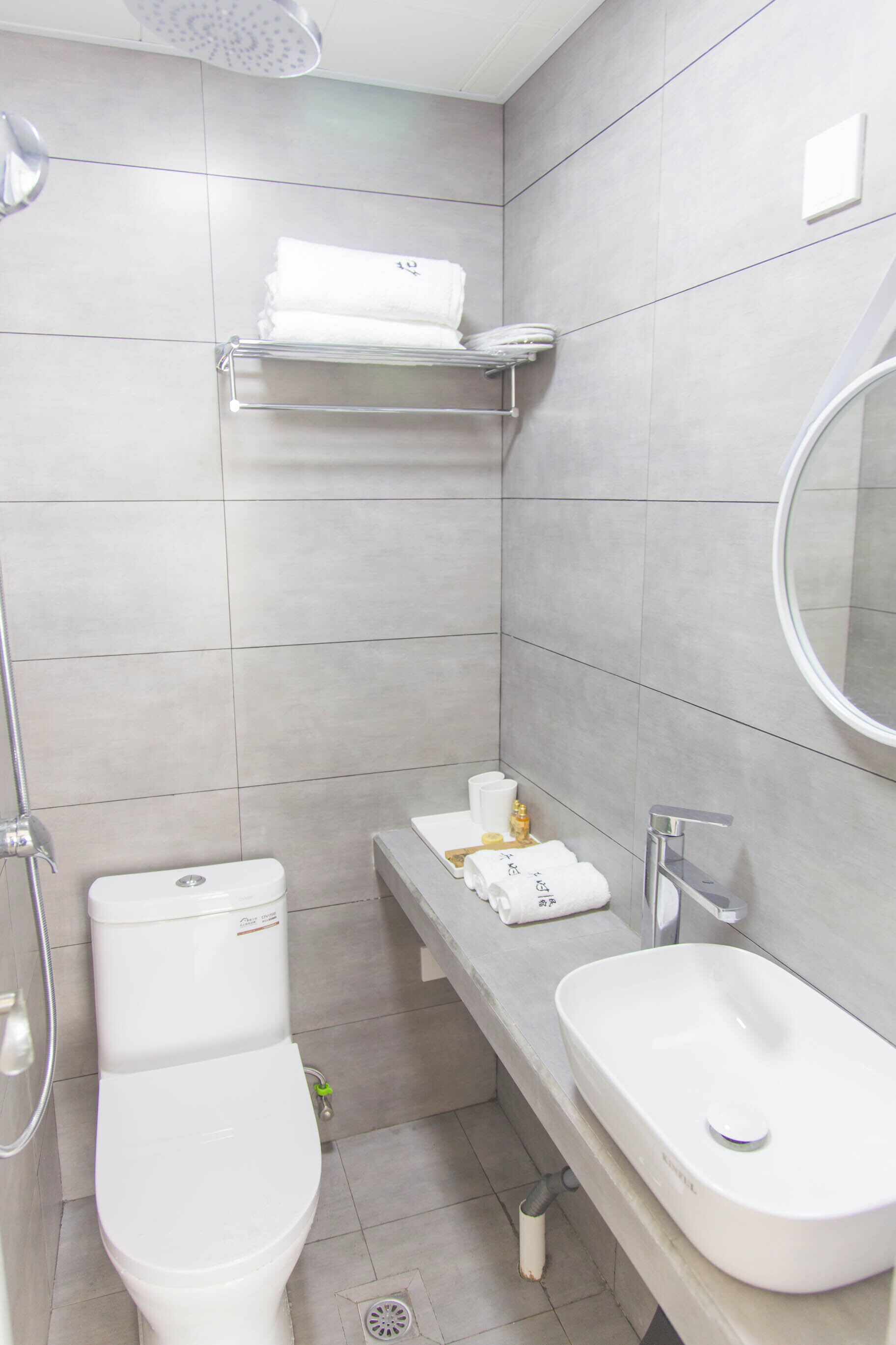 Un baño con inodoro, lavabo, ducha y perchero para toallas.